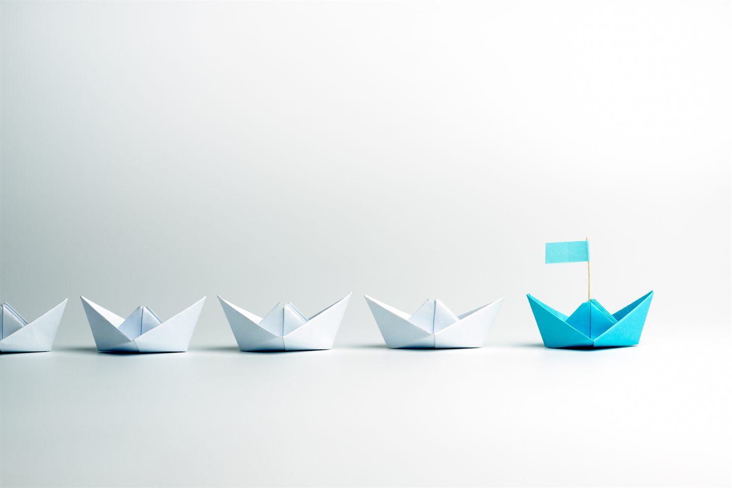 A blue paper boat leading a fleet of white boats: strategy is choosing the direction